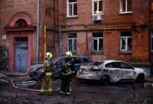 Bomberos junto a coches y un edificio de apartamentos dañados durante un ataque de drones rusos.