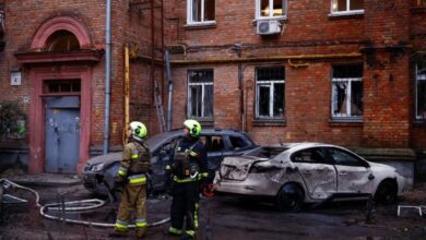 Bomberos junto a coches y un edificio de apartamentos dañados durante un ataque de drones rusos.