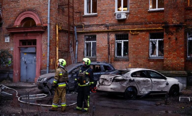 Bomberos junto a coches y un edificio de apartamentos dañados durante un ataque de drones rusos.