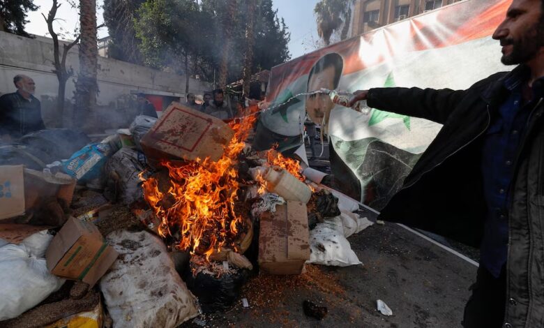 Una imagen del derrocado sirio Bashar al Assad arde en el fuego mientras un miembro sirio de las fuerzas rebeldes destruye drogas y bebidas alcohólicas encontradas en un edificio en Damasco (AP Foto/Omar Sanadiki)
