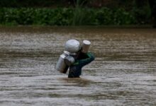 Un residente lleva cubos de leche mientras cruza una carretera inundada. Foto: Reuters