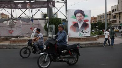 Varias personas circulan cerca de una pancarta con la imagen del líder supremo de Irán, Mojtaba Khamenei, en una calle de Teherán, Irán.